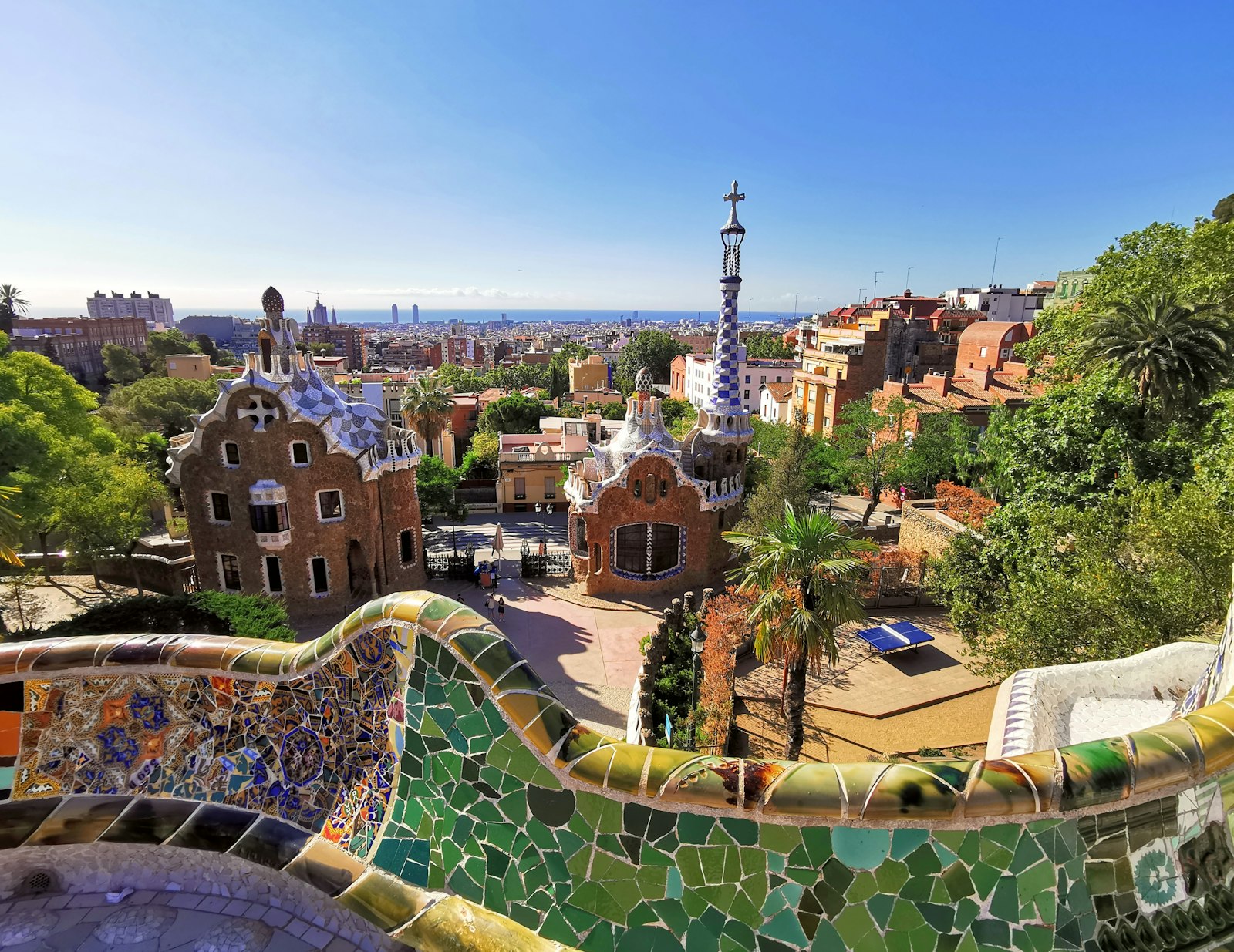Le parc Güell de Gaudí à Barcelone : le banc en mosaïque, les pavillons et la ville sous un ciel bleu.